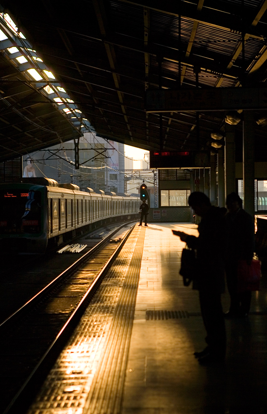Seoul subway platform with a train and passengers in backlight