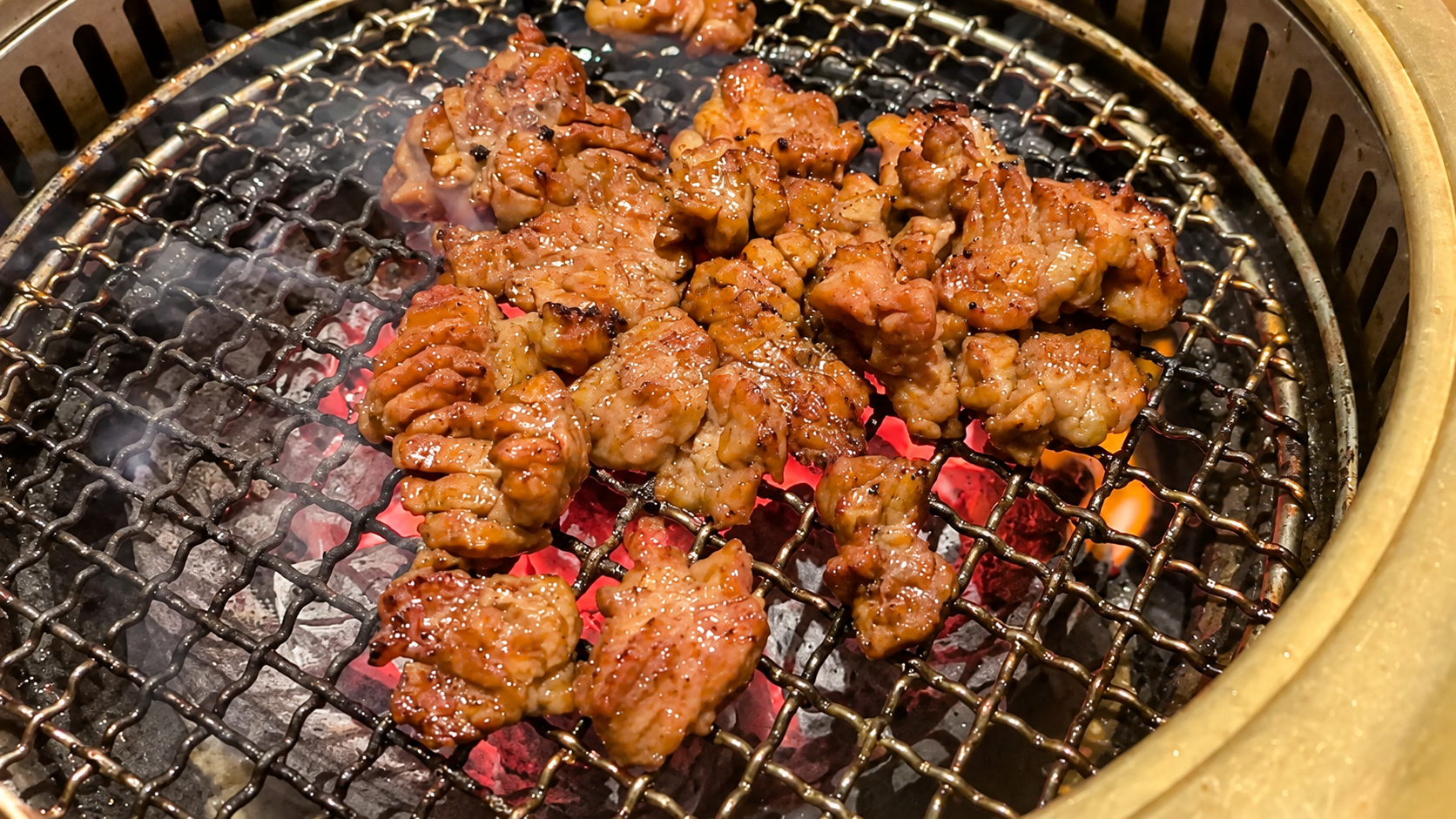 Marinated dwaeji-galbi grilling over glowing charcoal at a Korean barbecue restaurant.