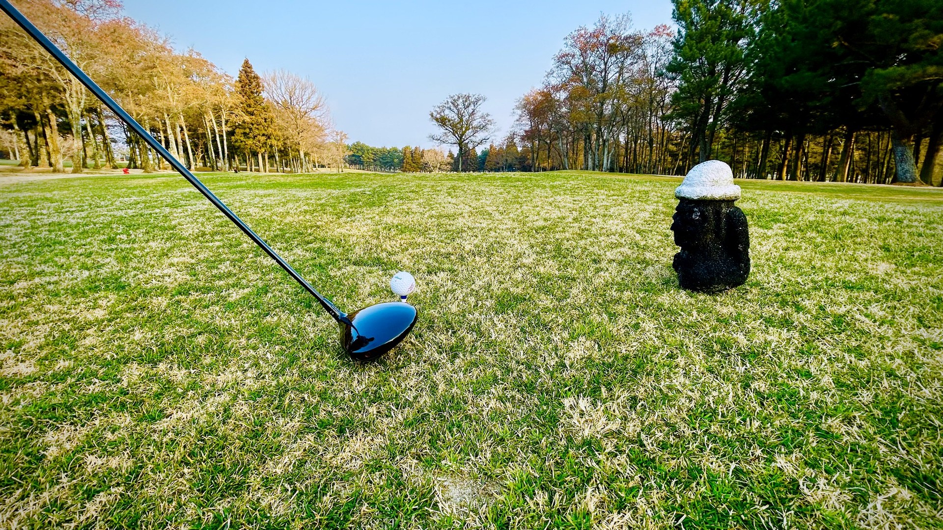 Golf ball on a tee beside a Jeju stone figure on a golf course
