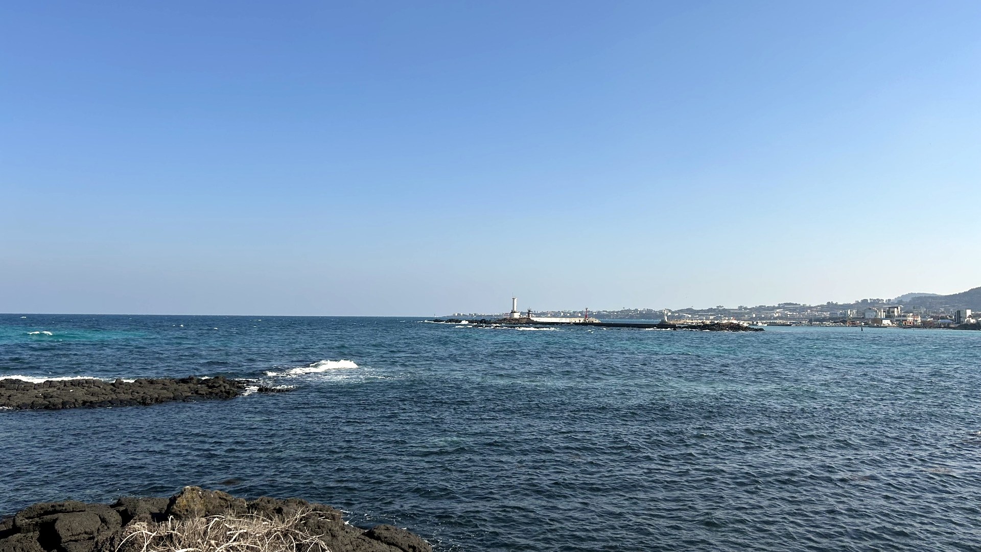 Jeju coastline with black volcanic rocks and a lighthouse